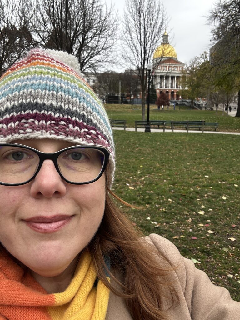 Katy with a multi colored hat on standing in front of a building with a gold dome -- She's in Boston here!